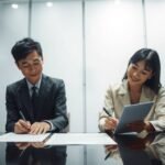 オフィスで書類に署名しようとしている2人の人物の画像