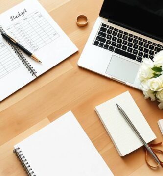 上から見た机のイメージ。ノートには英語で「Budget」と書かれており、鉛筆、花束、ノートパソコン、ハサミ、そして結婚指輪が置かれている。